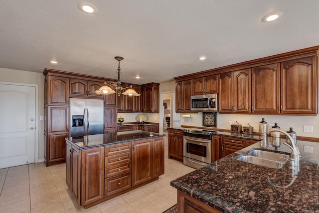 kitchen with pendant lighting, appliances with stainless steel finishes, a sink, a kitchen island, and dark stone counters