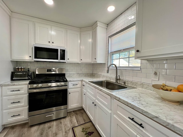 kitchen with tasteful backsplash, light wood-style floors, gas stove, white cabinets, and a sink