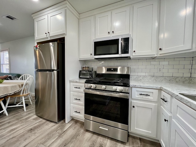 kitchen featuring light wood finished floors, stainless steel appliances, visible vents, decorative backsplash, and white cabinetry