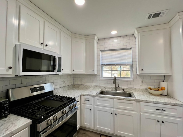 kitchen featuring visible vents, white microwave, gas stove, white cabinets, and a sink