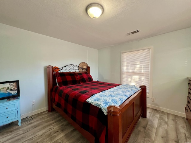 bedroom featuring light wood finished floors, baseboards, visible vents, and a textured ceiling