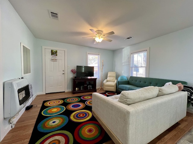 living room with ceiling fan, wood finished floors, visible vents, and heating unit