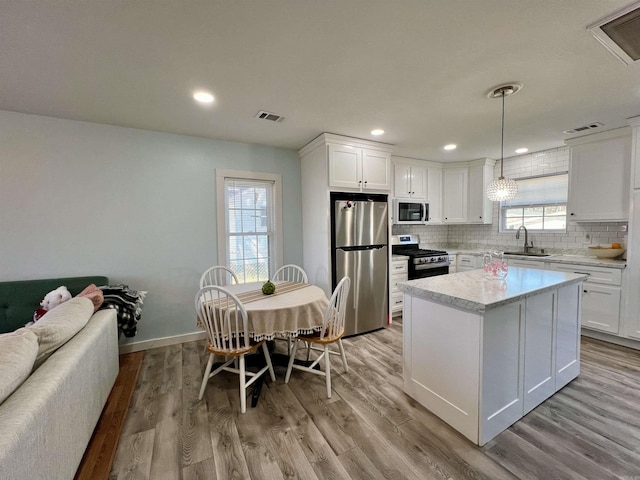 kitchen featuring light wood-type flooring, decorative backsplash, stainless steel appliances, and a sink