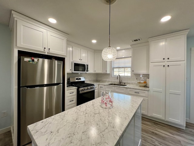 kitchen with stainless steel appliances, a sink, visible vents, white cabinets, and backsplash