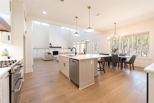 kitchen featuring appliances with stainless steel finishes, light wood-style floors, a fireplace, white cabinetry, and a sink