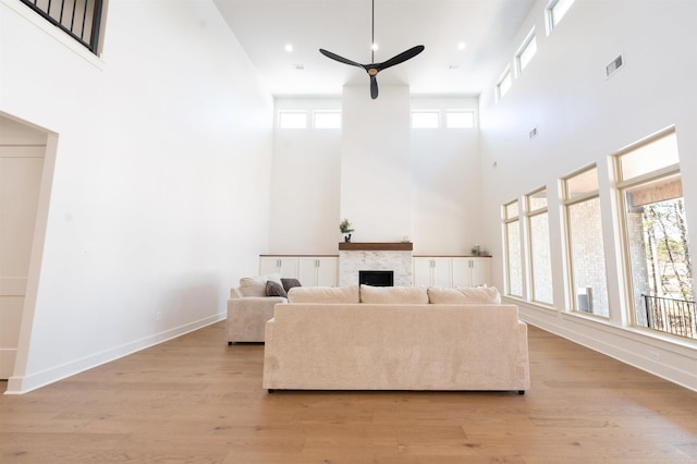 living area featuring baseboards, visible vents, ceiling fan, light wood-style floors, and a fireplace