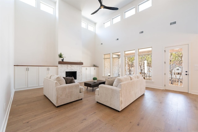 living area with light wood-style floors, a fireplace, visible vents, and a ceiling fan