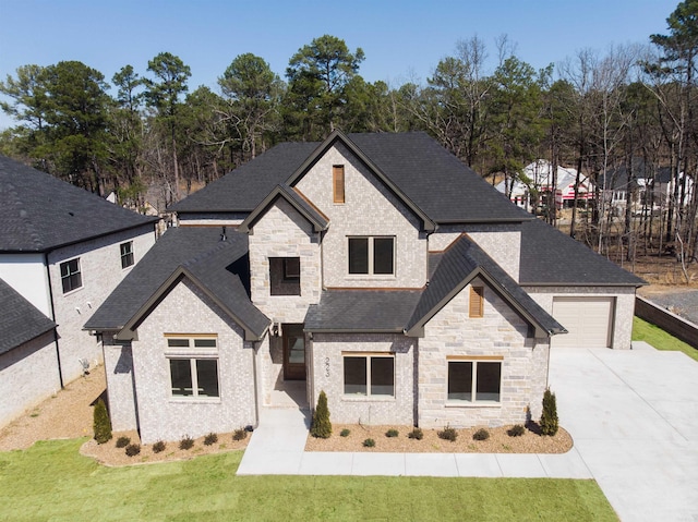 french country inspired facade with driveway, stone siding, roof with shingles, and a front yard