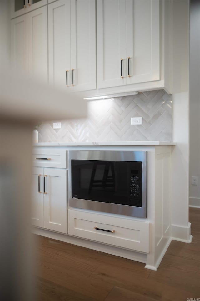 details with stainless steel microwave, dark wood finished floors, backsplash, and white cabinetry