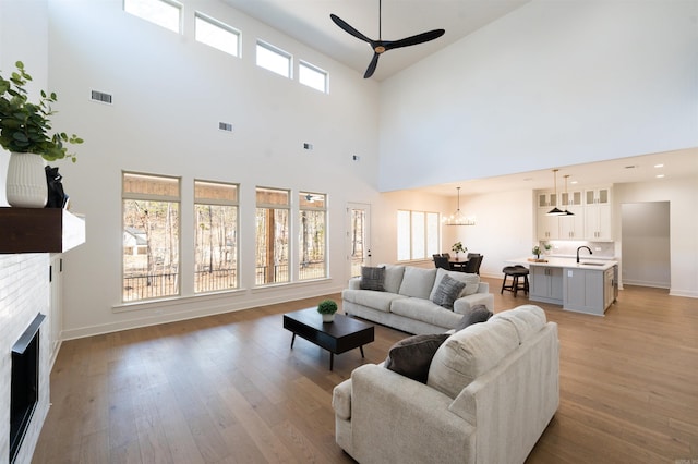 living room with visible vents, a fireplace, light wood finished floors, and ceiling fan with notable chandelier