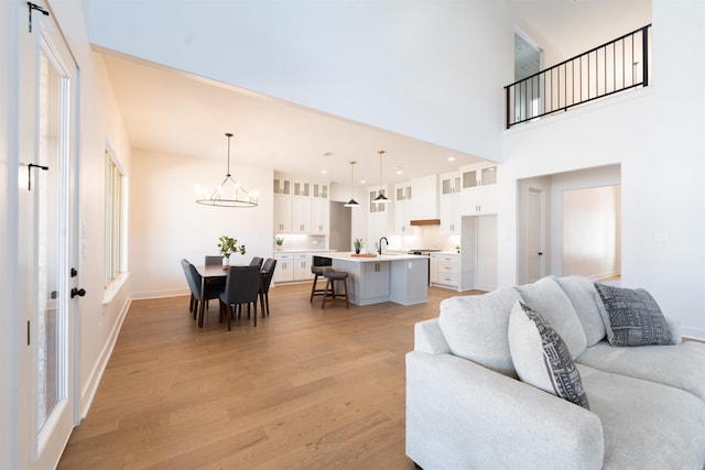 living area with recessed lighting, a towering ceiling, light wood-style flooring, a chandelier, and baseboards