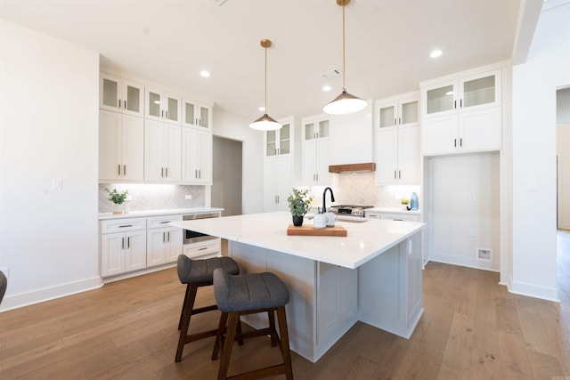 kitchen featuring an island with sink, light wood finished floors, custom range hood, and white cabinetry