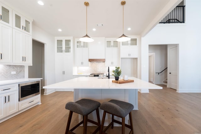 kitchen featuring light wood finished floors, stainless steel microwave, white cabinetry, premium range hood, and a kitchen breakfast bar