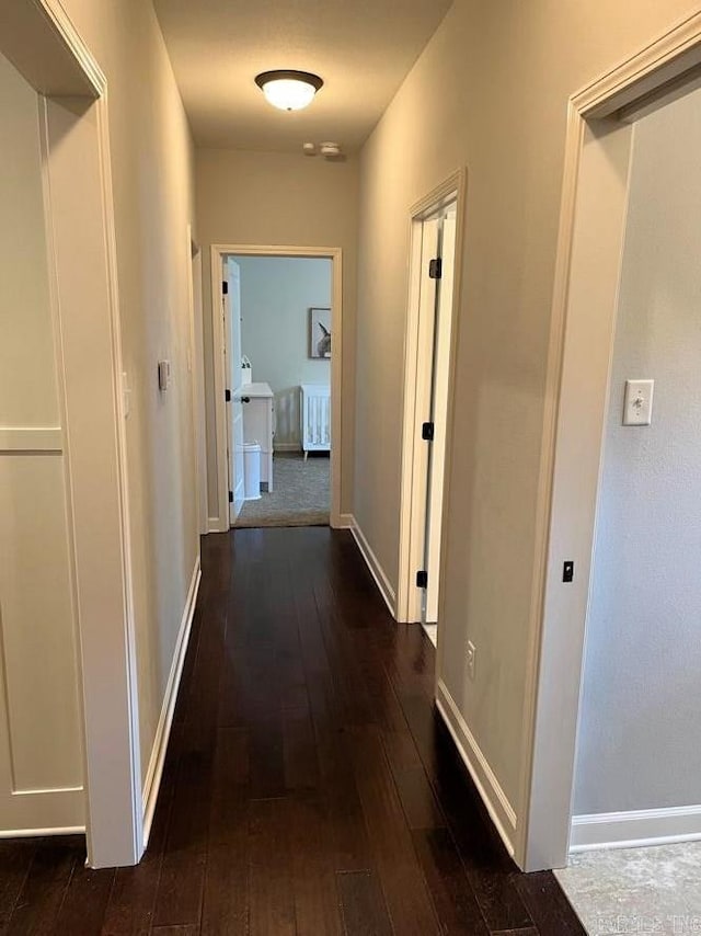 hallway featuring dark wood-style flooring and baseboards