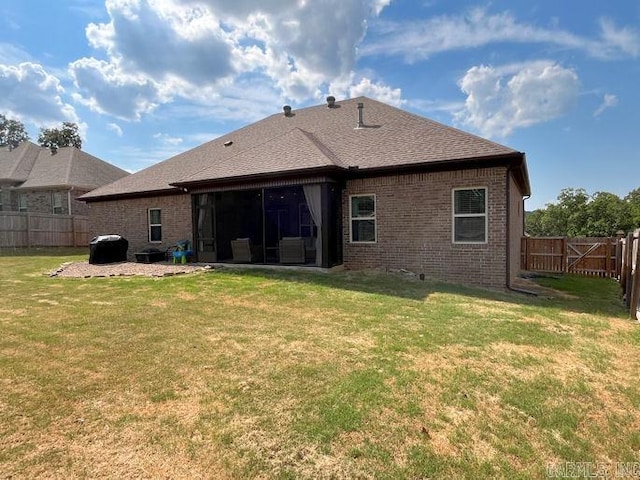 back of property featuring brick siding, roof with shingles, a lawn, a sunroom, and a fenced backyard