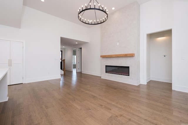 unfurnished living room featuring a large fireplace, a towering ceiling, baseboards, and wood finished floors