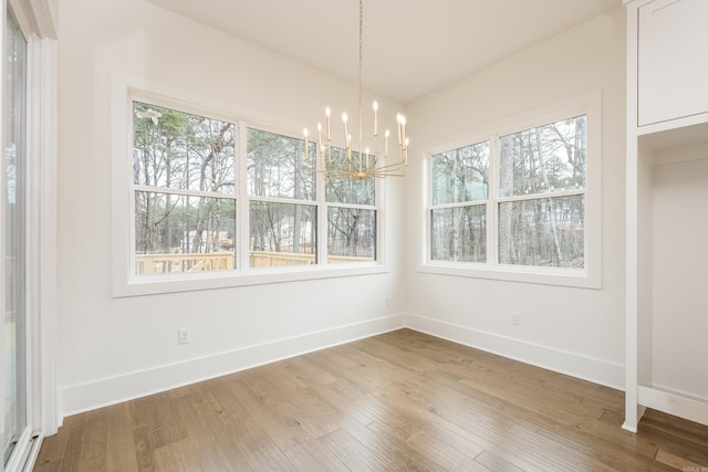 unfurnished dining area featuring an inviting chandelier, wood finished floors, and baseboards