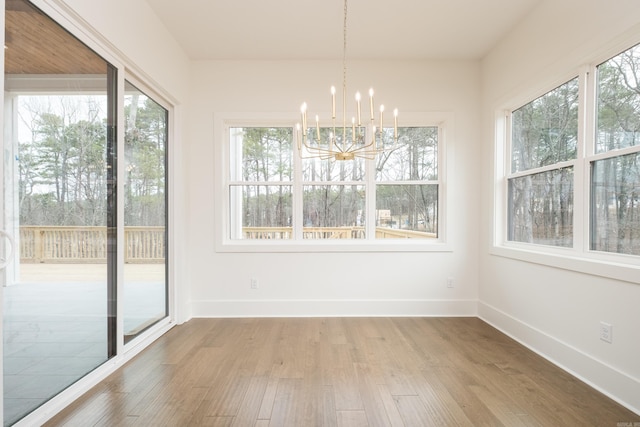 unfurnished dining area with a notable chandelier, baseboards, and wood finished floors