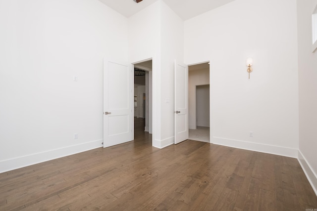 empty room featuring wood finished floors, a towering ceiling, and baseboards