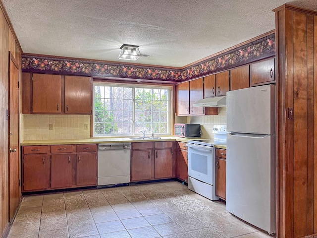 kitchen featuring light countertops, decorative backsplash, a sink, white appliances, and under cabinet range hood