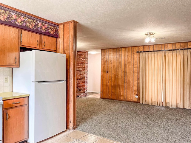 kitchen featuring freestanding refrigerator, light colored carpet, wooden walls, and a textured ceiling