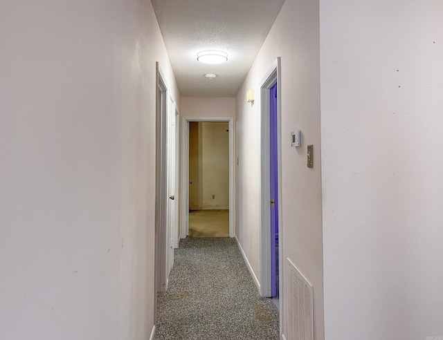 hallway with a textured ceiling, baseboards, visible vents, and light colored carpet