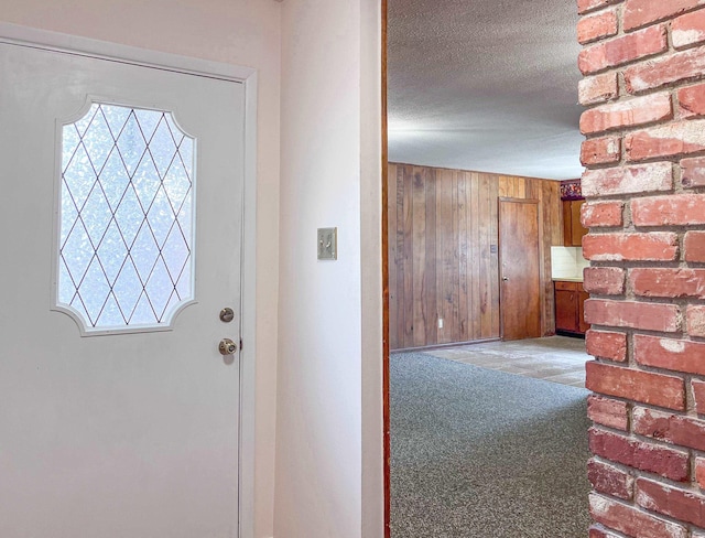 entryway with wood walls, a textured ceiling, and carpet flooring