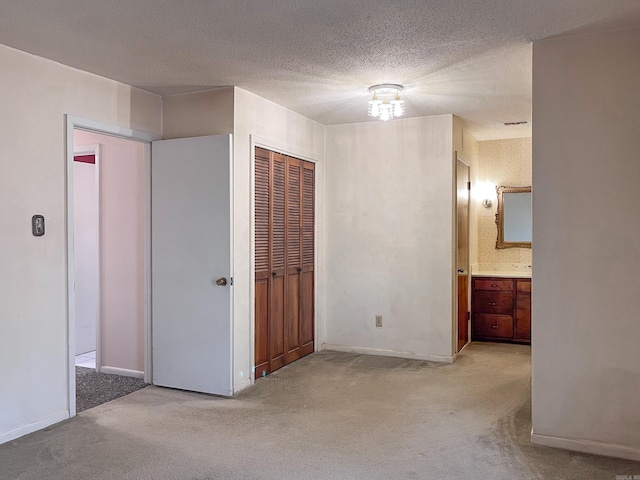 unfurnished bedroom featuring light carpet, visible vents, ensuite bathroom, a textured ceiling, and a closet