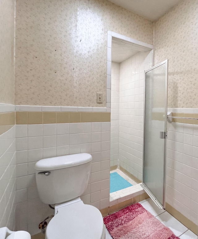 full bath with wallpapered walls, a shower stall, tile walls, and a wainscoted wall