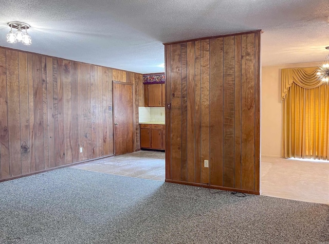 carpeted spare room with wooden walls, a chandelier, and a textured ceiling