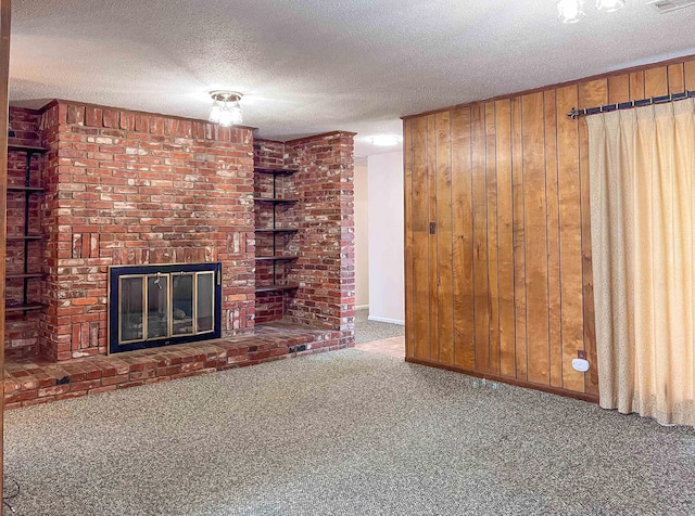 unfurnished living room featuring a textured ceiling, carpet floors, wood walls, visible vents, and a brick fireplace