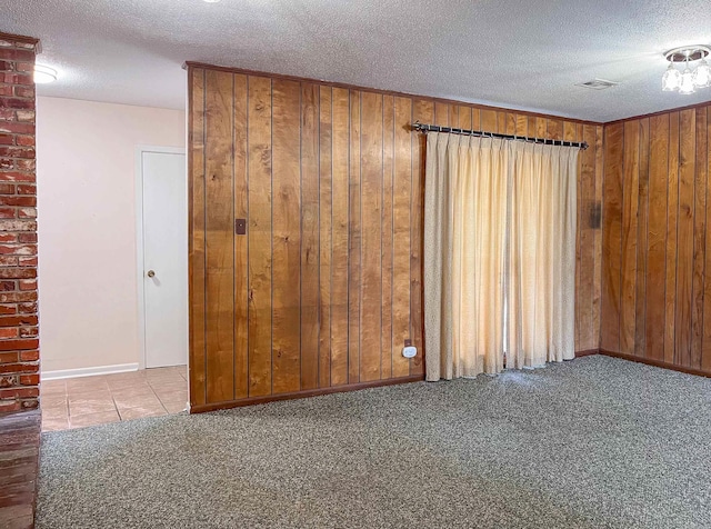 carpeted empty room featuring baseboards, wooden walls, and a textured ceiling