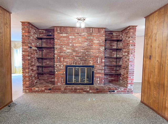 unfurnished living room featuring wooden walls, carpet flooring, a fireplace, and a textured ceiling