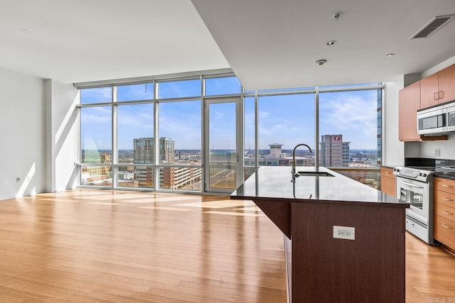 kitchen with a city view, stainless steel appliances, visible vents, light wood-style flooring, and a wall of windows