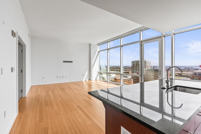 interior space with dark stone counters, wood finished floors, a view of city, expansive windows, and a sink