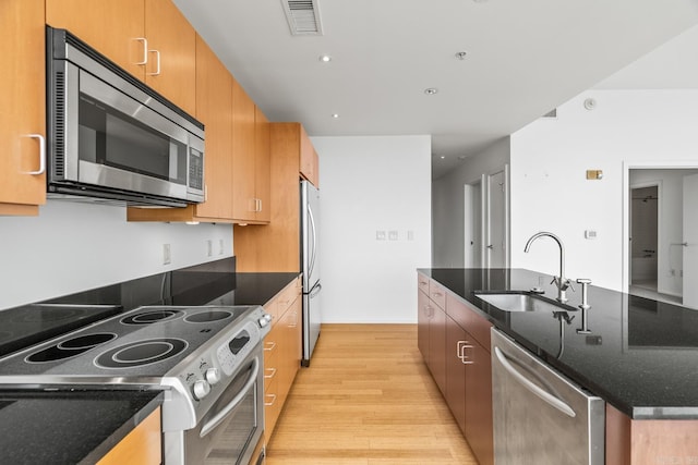 kitchen with stainless steel appliances, a sink, visible vents, light wood finished floors, and an island with sink