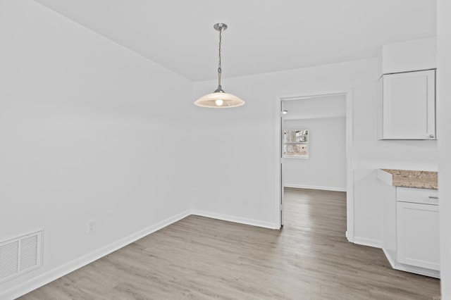 unfurnished dining area featuring light wood-style floors, visible vents, and baseboards