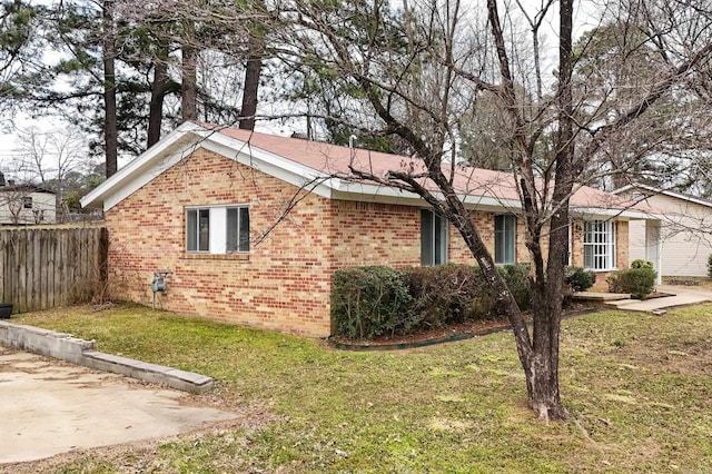 view of property exterior with brick siding, a lawn, and fence