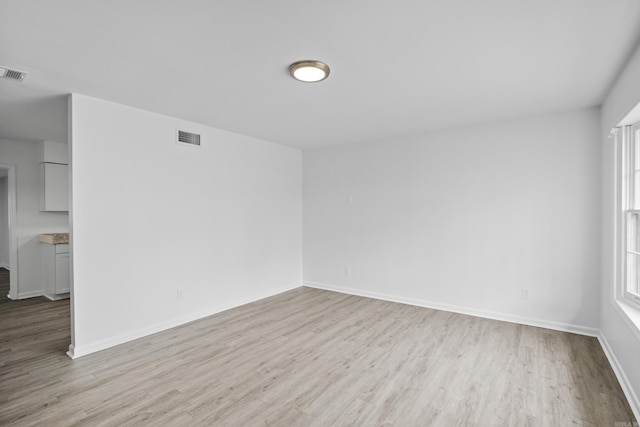 empty room featuring light wood-style floors, visible vents, and baseboards