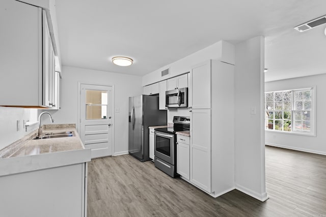 kitchen featuring stainless steel appliances, a sink, visible vents, light countertops, and light wood-type flooring