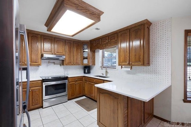 kitchen featuring light tile patterned floors, a peninsula, stainless steel appliances, under cabinet range hood, and a sink