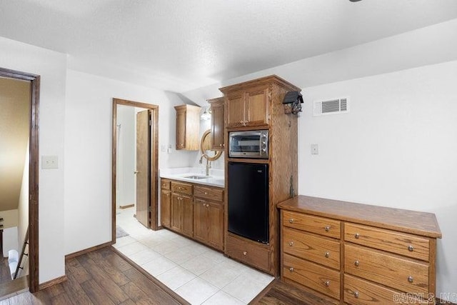 kitchen with light wood-style flooring, a sink, visible vents, brown cabinets, and stainless steel microwave