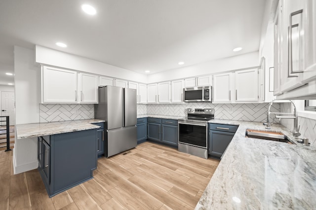 kitchen with stainless steel appliances, blue cabinets, white cabinets, and light stone countertops