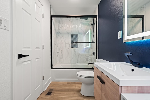 bathroom featuring enclosed tub / shower combo, toilet, wood finished floors, vanity, and visible vents