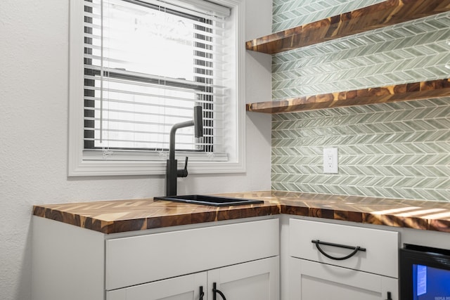 kitchen with open shelves, butcher block counters, a textured wall, white cabinets, and a sink