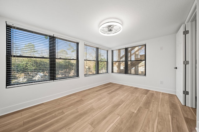 empty room featuring light wood-type flooring, a textured ceiling, and baseboards