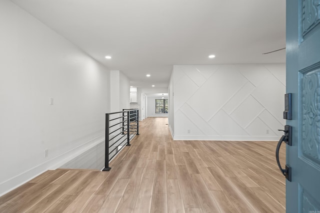 interior space featuring light wood finished floors, baseboards, a decorative wall, and recessed lighting