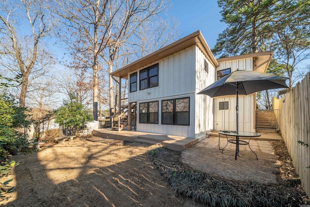 rear view of house with board and batten siding, fence, a patio, and stairs