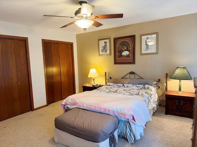 bedroom featuring a textured ceiling, multiple closets, a ceiling fan, and light colored carpet