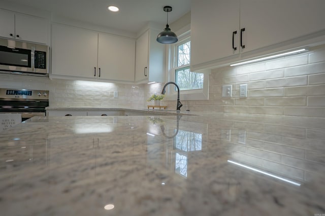 kitchen featuring appliances with stainless steel finishes, backsplash, hanging light fixtures, white cabinetry, and a sink